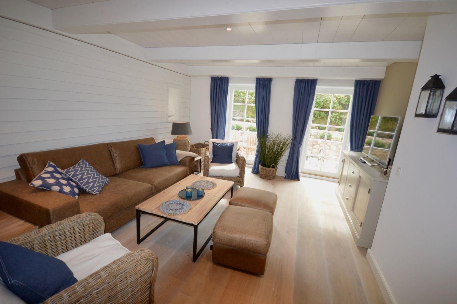 Wohnzimmer mit braunem Sofa, Holztisch und blauen Vorhängen vor Fenstern.