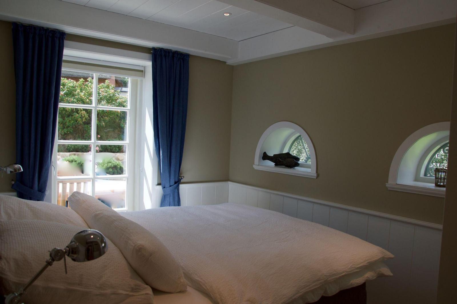 Schlafzimmer mit Bett, Fenster und zwei Bogenfenstern.