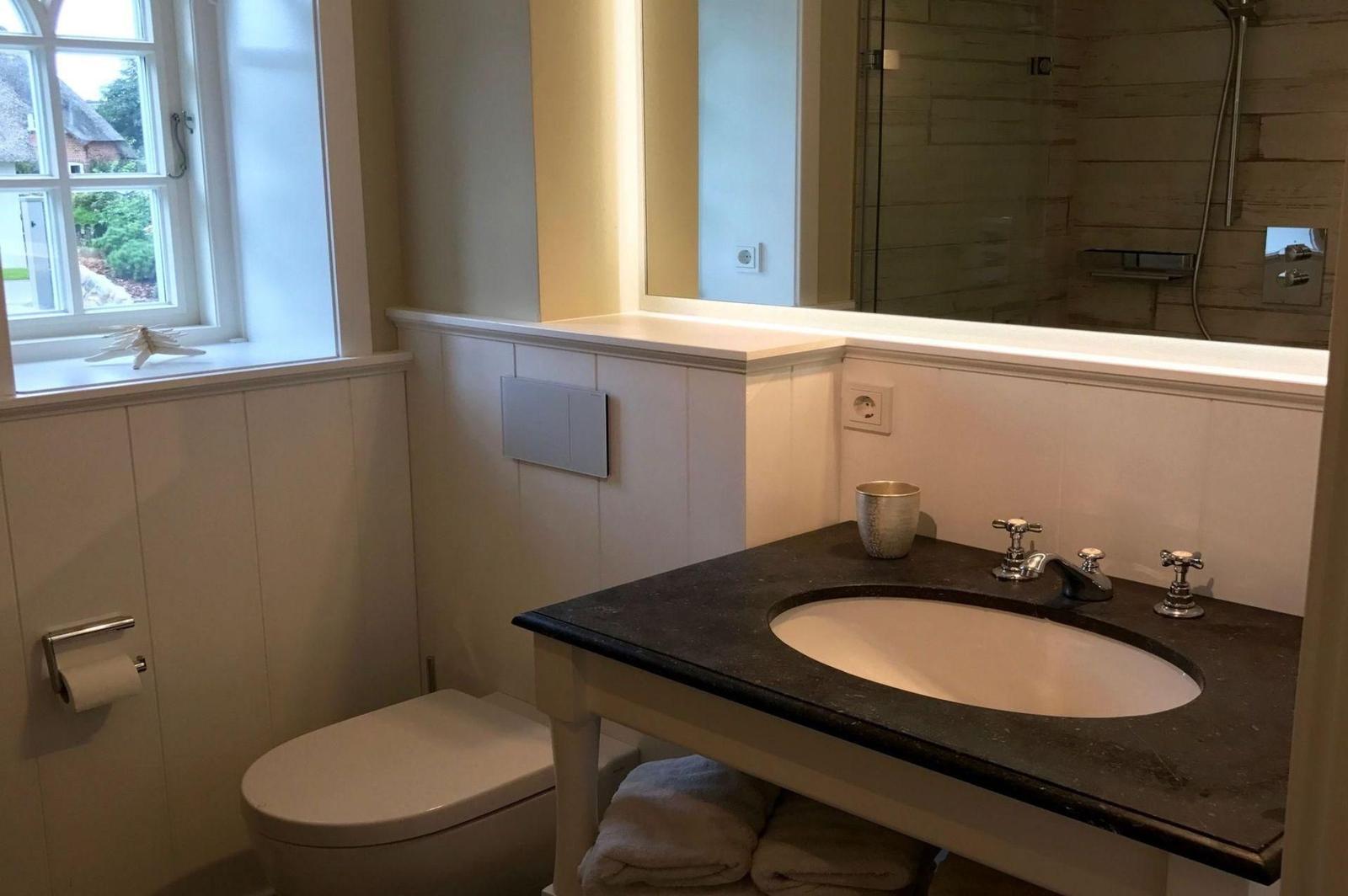 Badezimmer mit Waschbecken, Toilette und Dusche. Fenster mit Blick auf Garten.