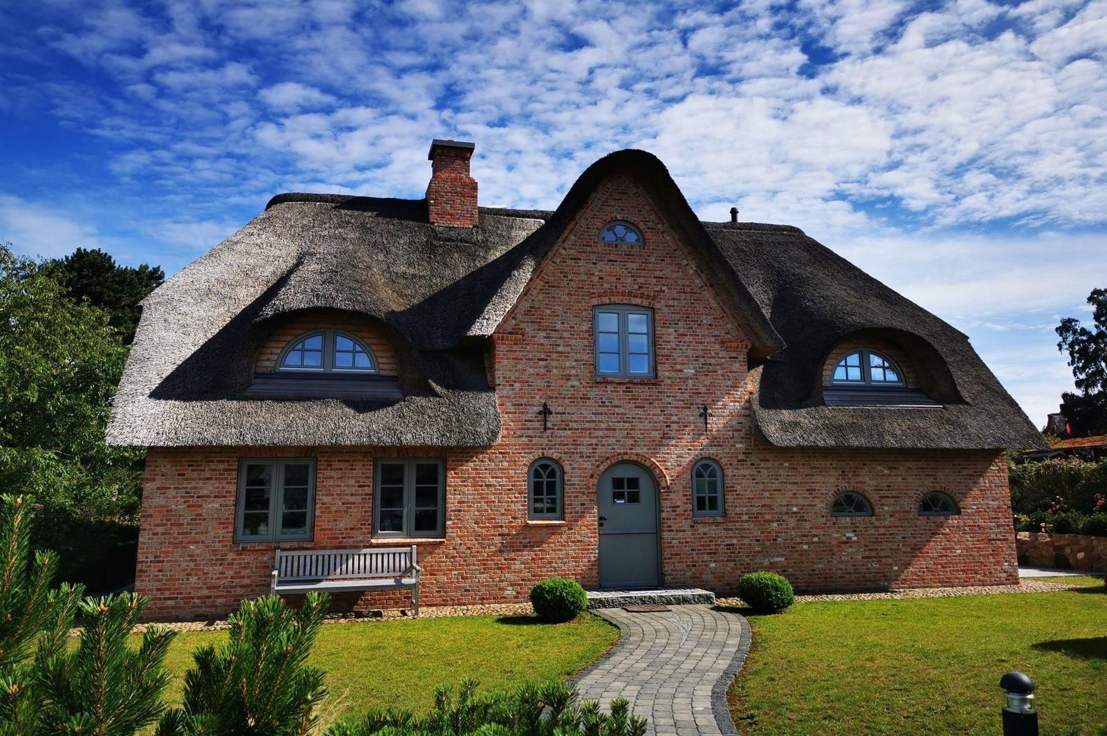 Haus mit Strohdach, Backsteinfassade und grüner Rasenfläche.