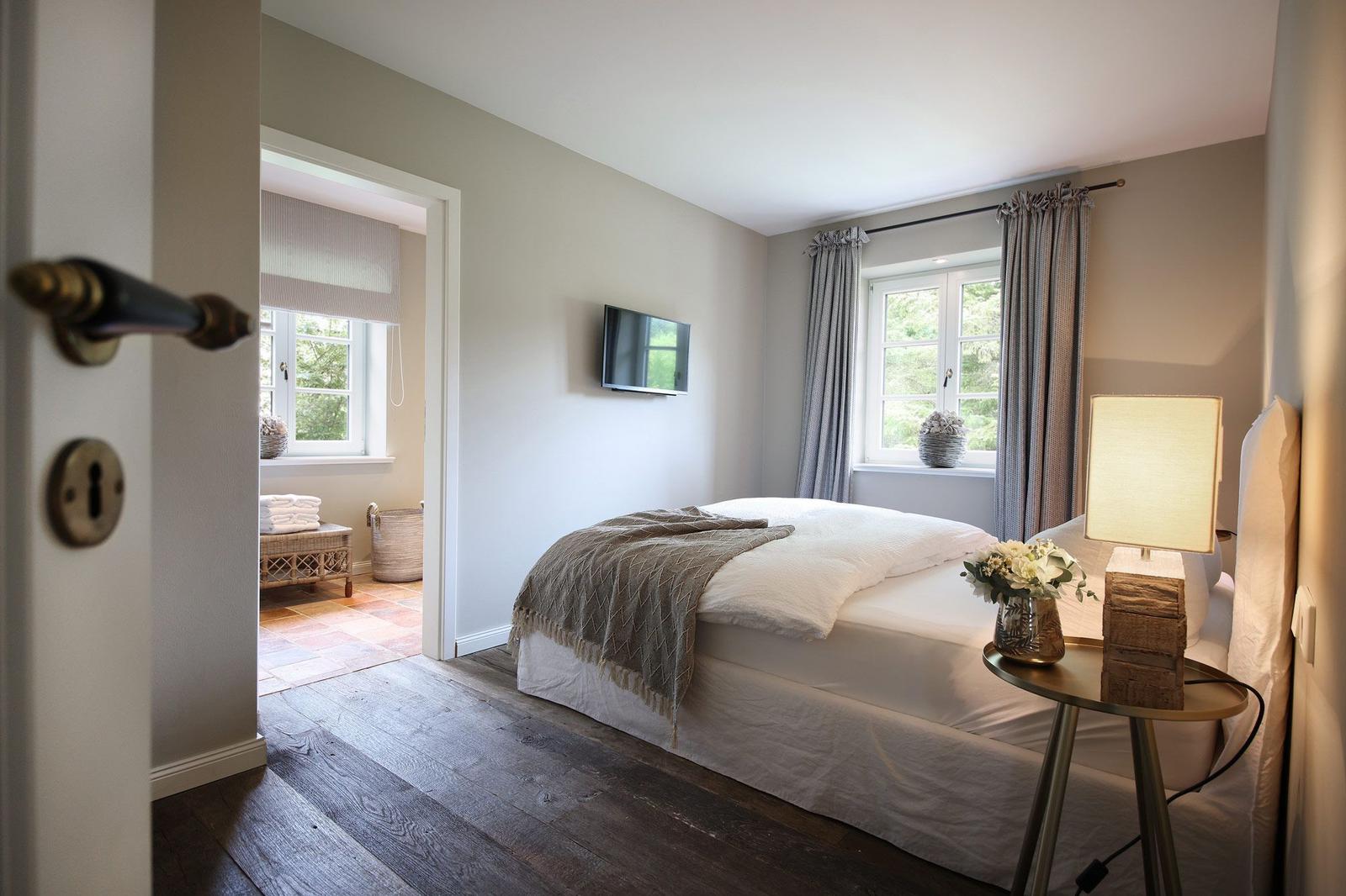 Schlafzimmer mit Bett, TV und Fenster. Holzfußboden und Nachttisch mit Lampe.
