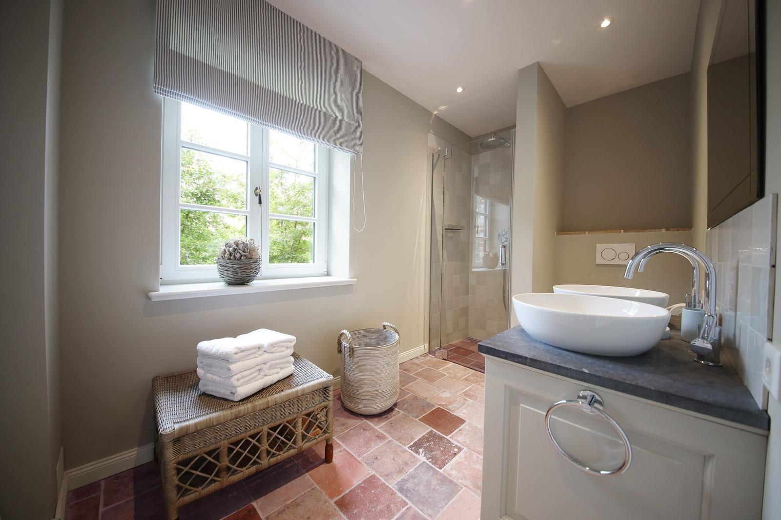 Badezimmer mit Dusche, Waschbecken und Fenster mit Blick auf Grün.