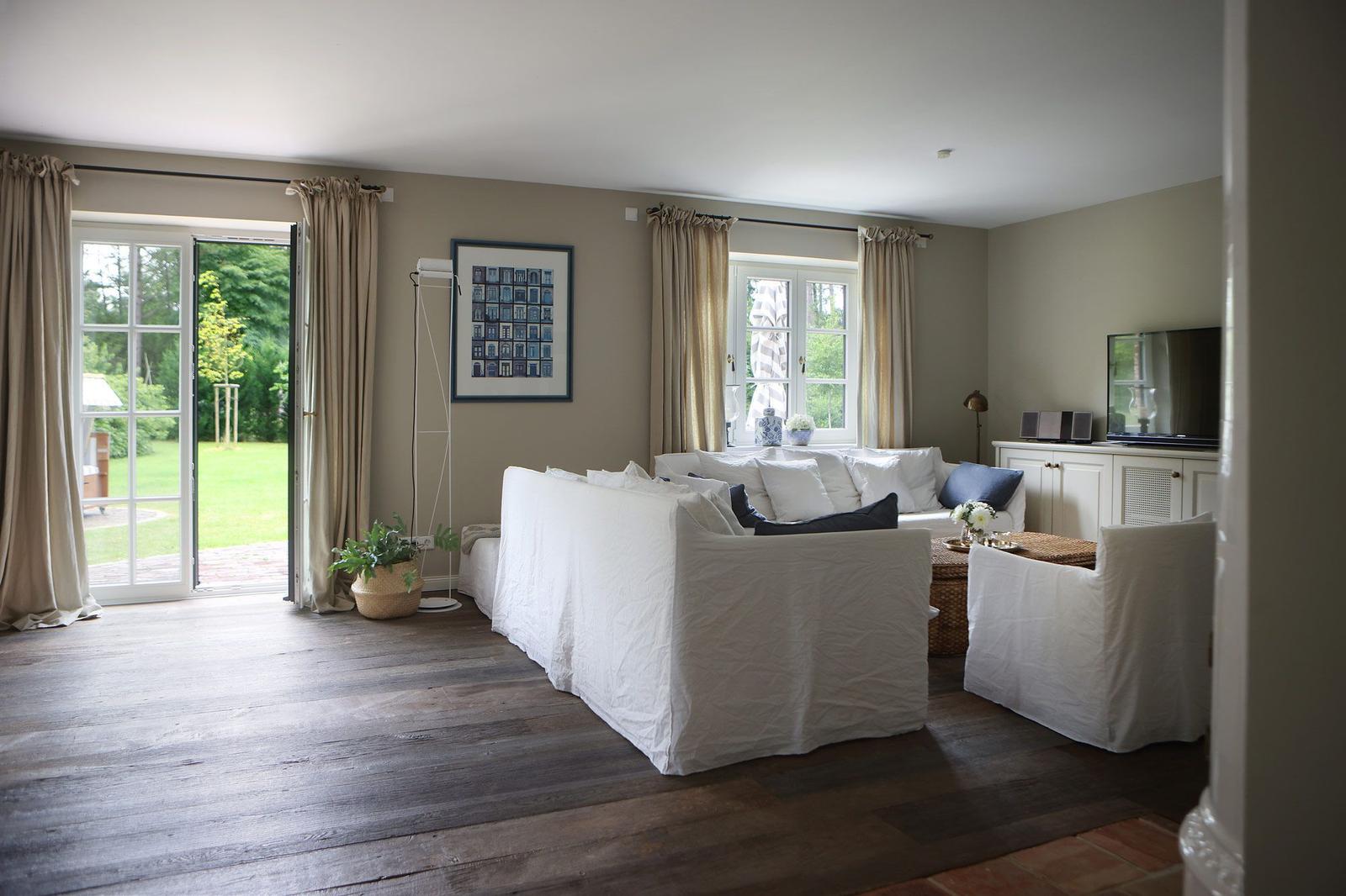 Wohnzimmer mit weißem Sofa, Holzboden und Blick auf Garten.