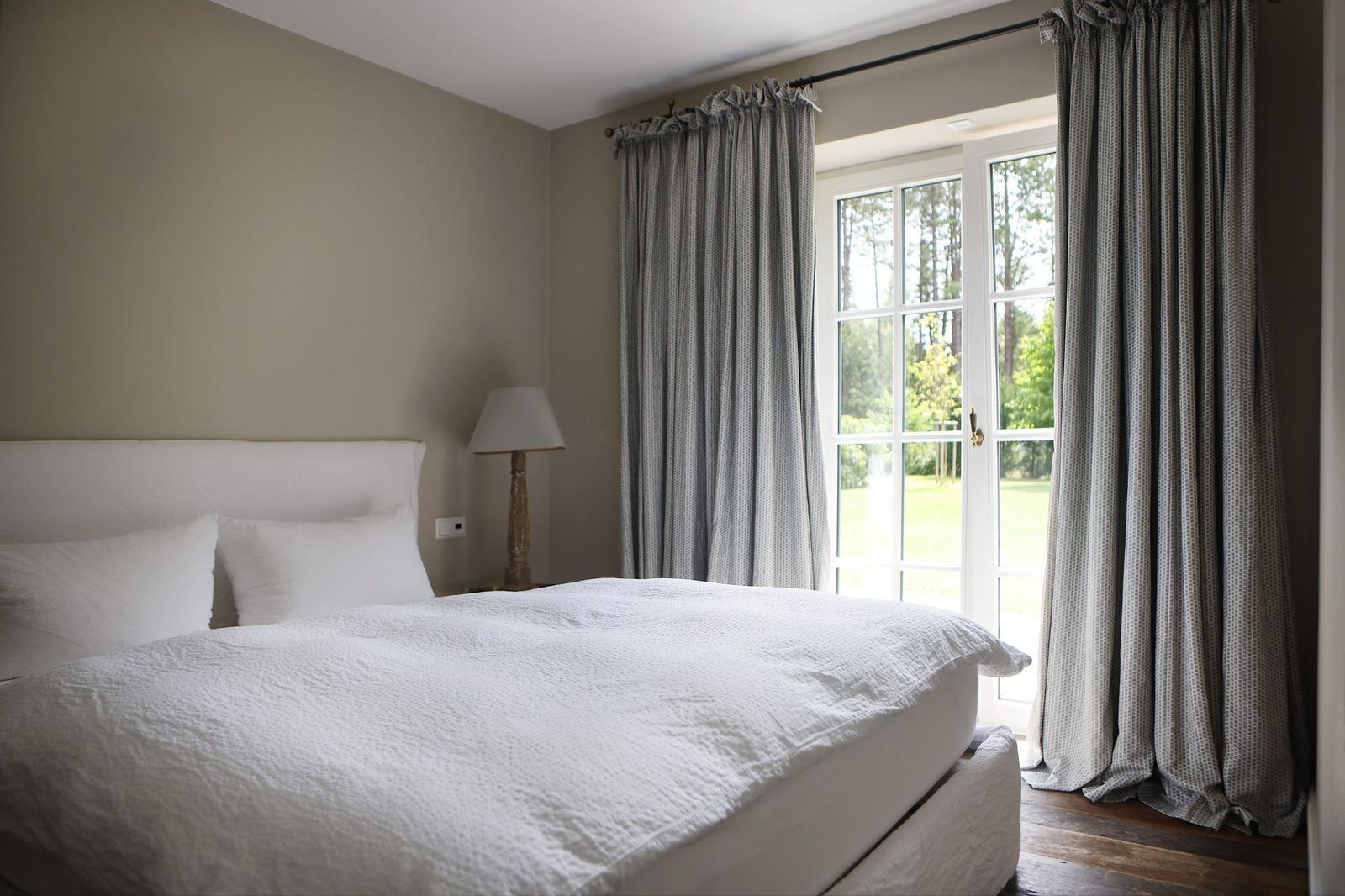 Schlafzimmer mit weißem Bett und Fenster zur grünen Außenseite.