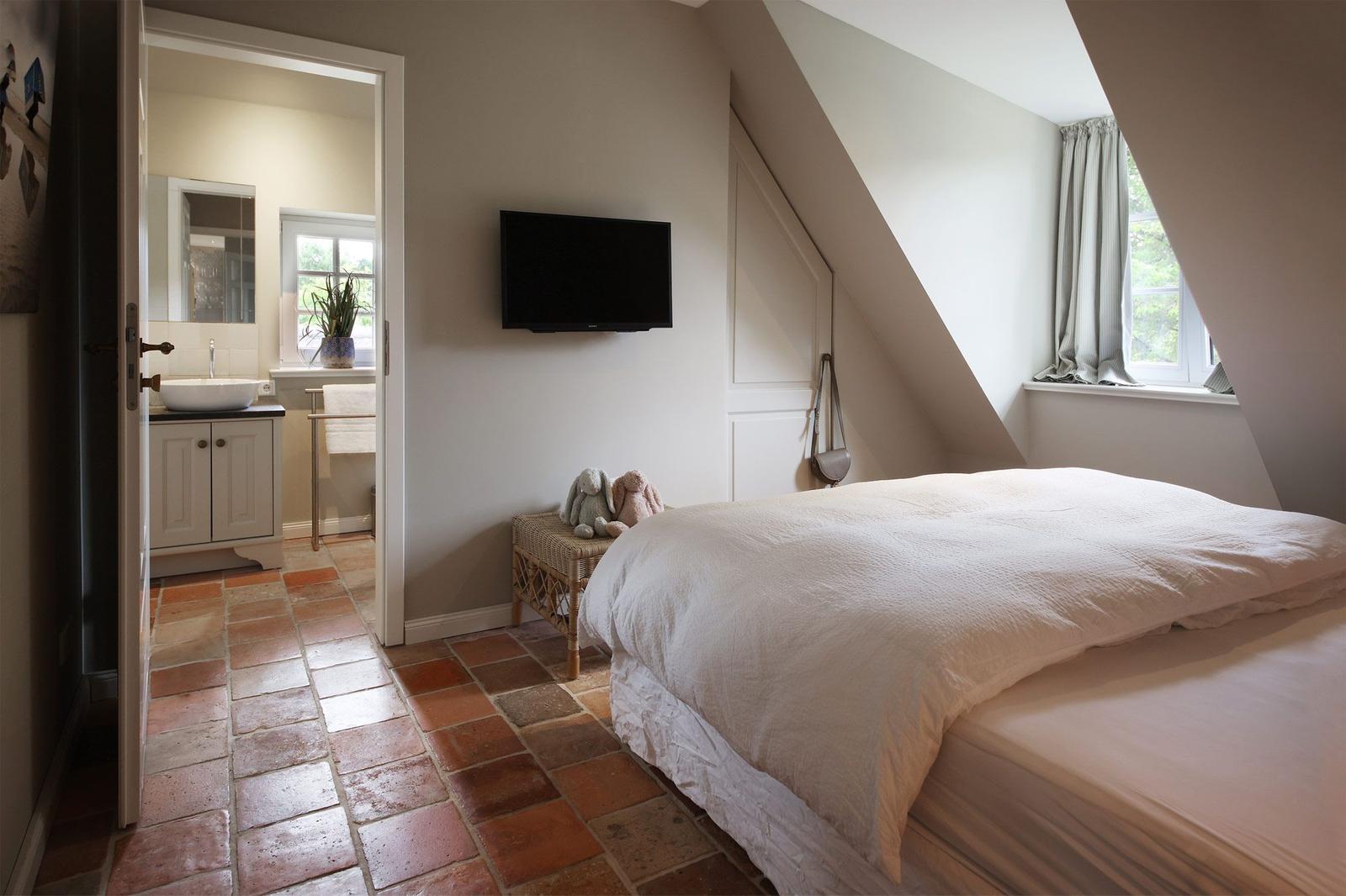 Schlafzimmer mit Dachschrägen, Bett, Fernseher und Tür zum Badezimmer.