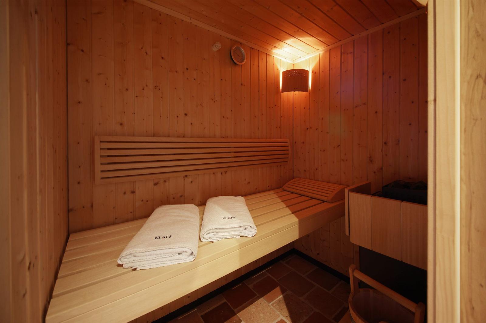 Sauna mit Holzbank, zwei Handtüchern und Wandbeleuchtung.