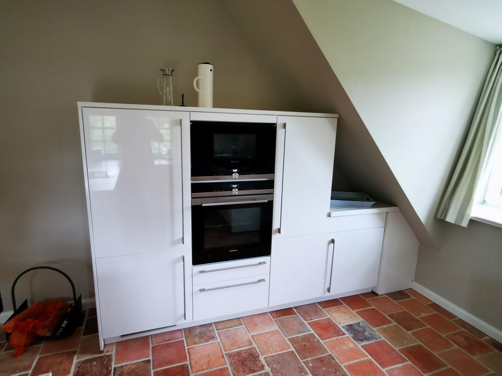 Küche mit weißer Einbauküche und integriertem Backofen unter schrägem Dach.