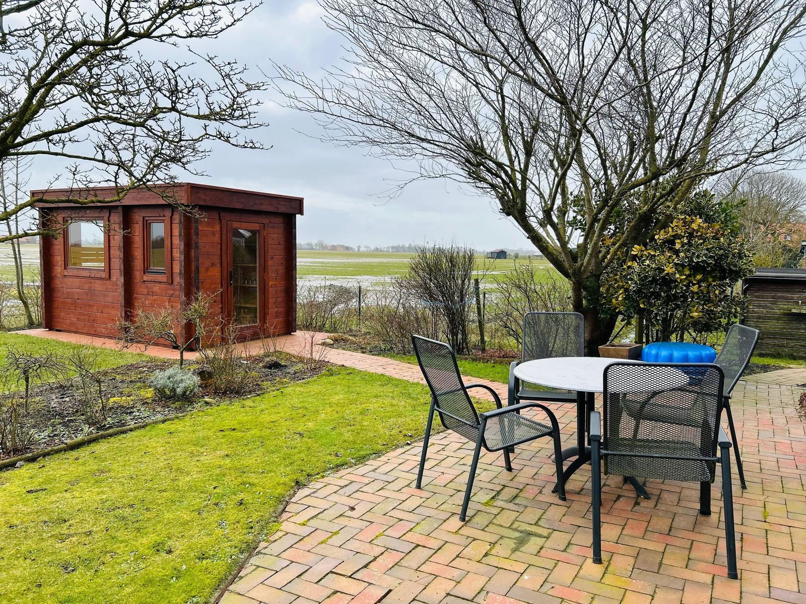 Holzhaus mit Garten, Tisch und Stühlen. Blick auf Felder und Bäume.