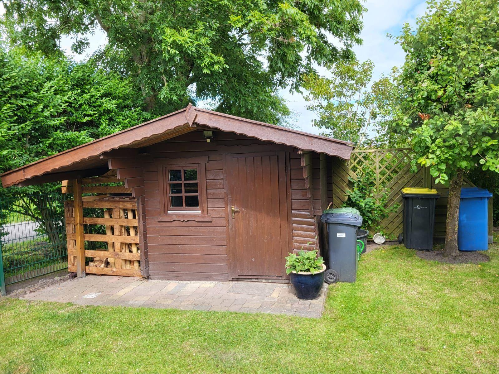 Holzgarage mit Dachüberstand und Mülltonnen im Garten.