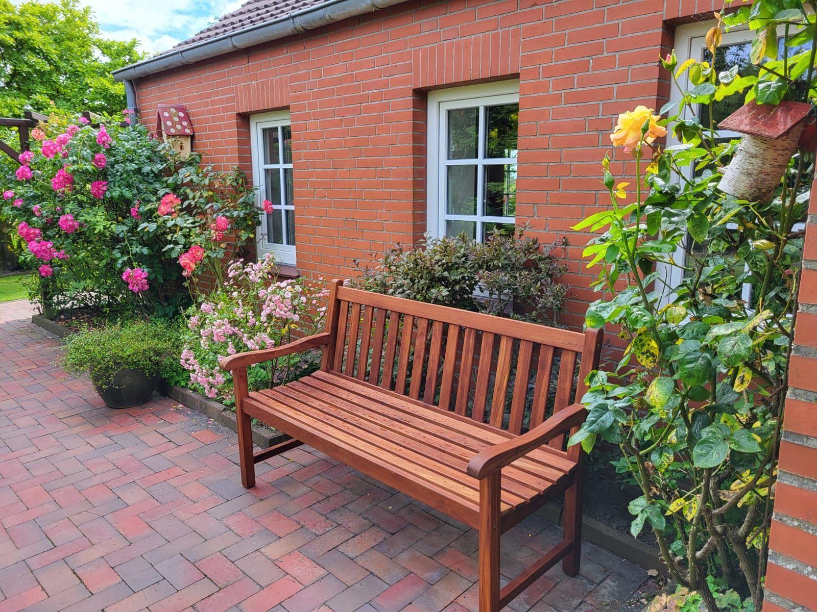 Holzbank auf gepflasterter Terrasse vor rotem Backsteinhaus mit Rosenbeete und Fenstern.