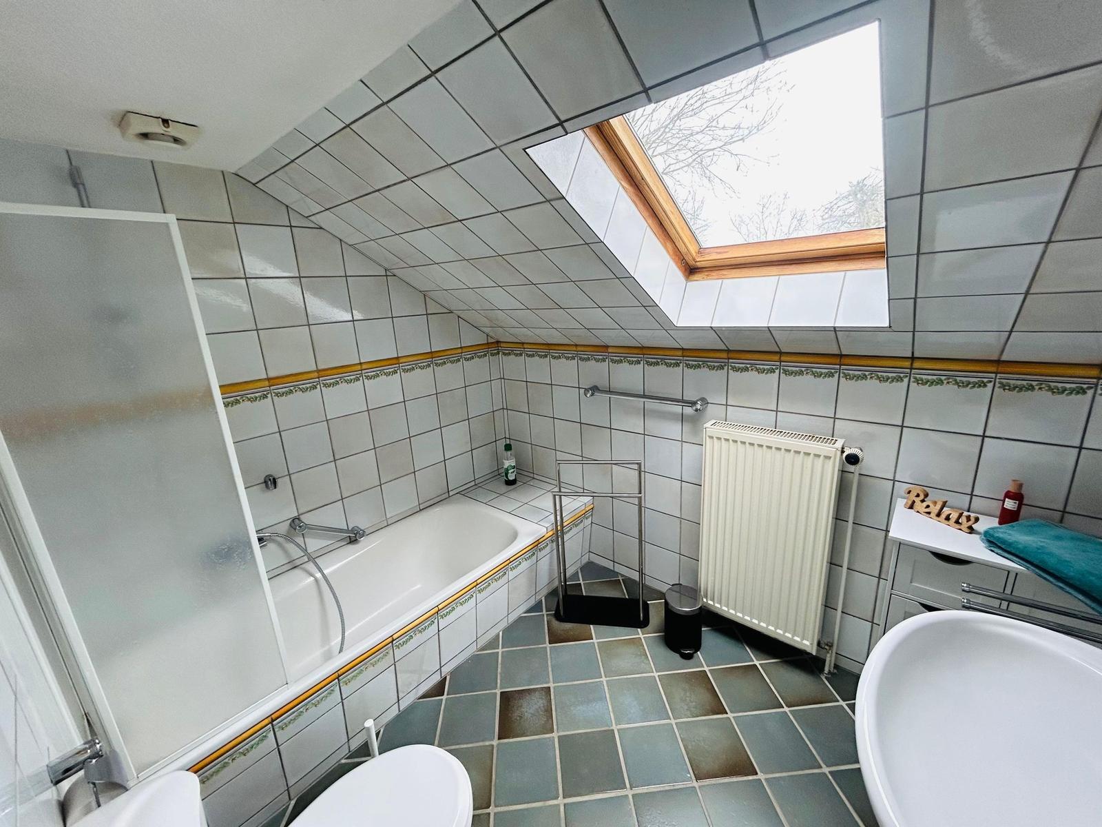 Badezimmer mit Dusche, Badewanne, Toilette und Waschbecken unter Dachschrägen mit Dachfenster.
