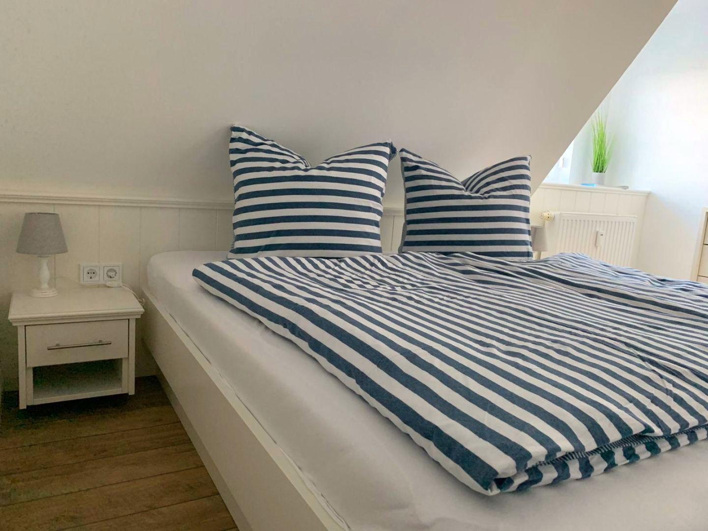 Schlafzimmer mit Bett, Kissen und Nachttisch unter schräger Decke.