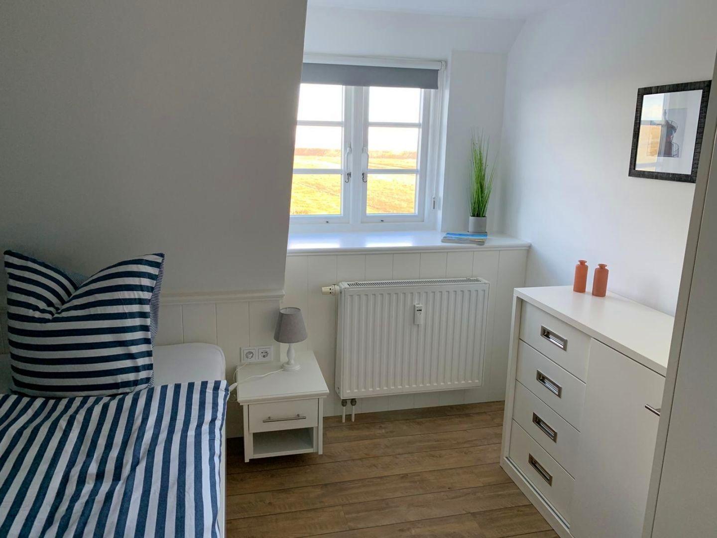 Schlafzimmer mit Bett, Nachttisch und Schrank. Fenster mit Blick auf Feld.