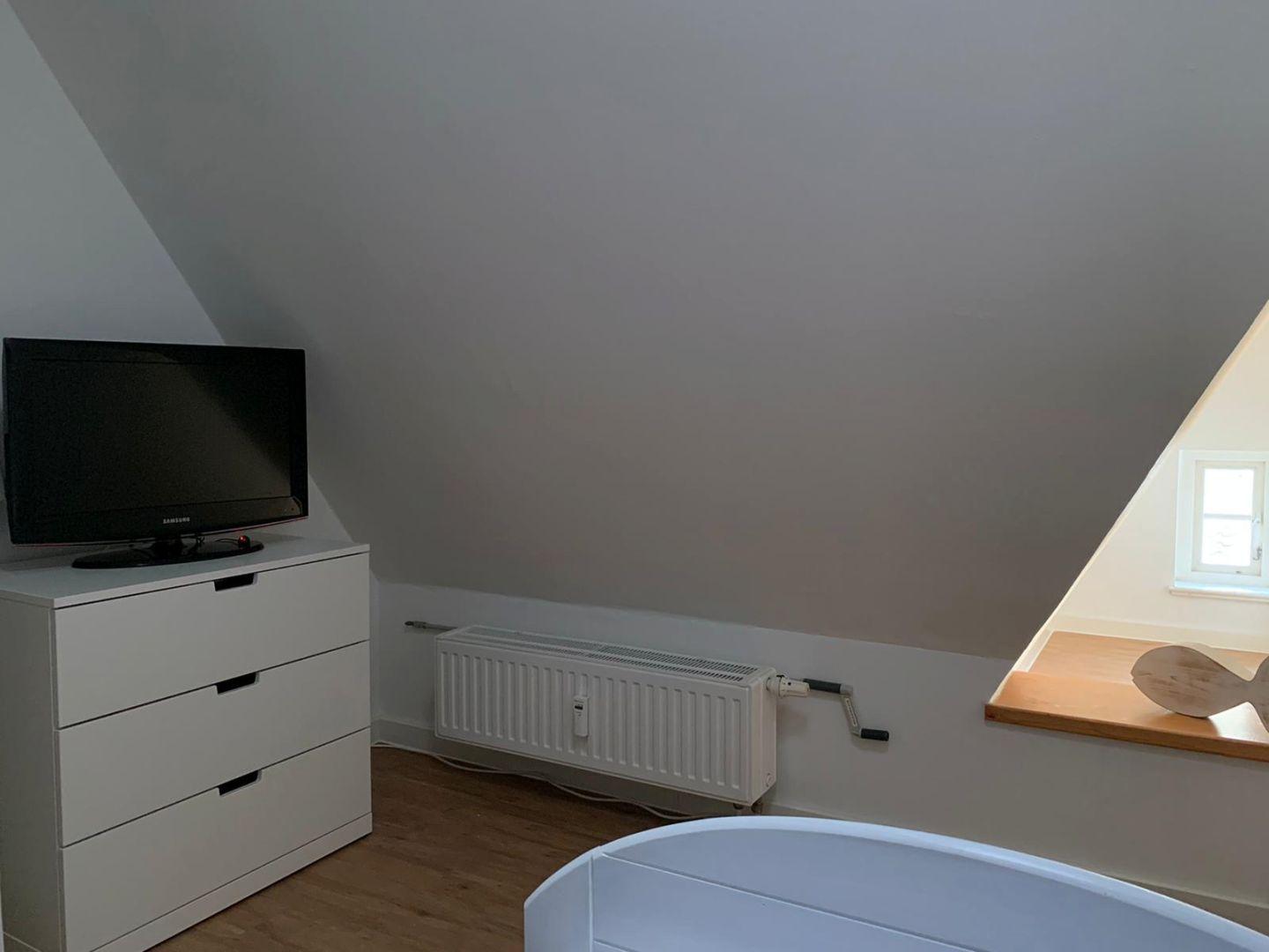 Zimmer mit schrägen Wänden, Fernseher, Heizkörper und Fenster