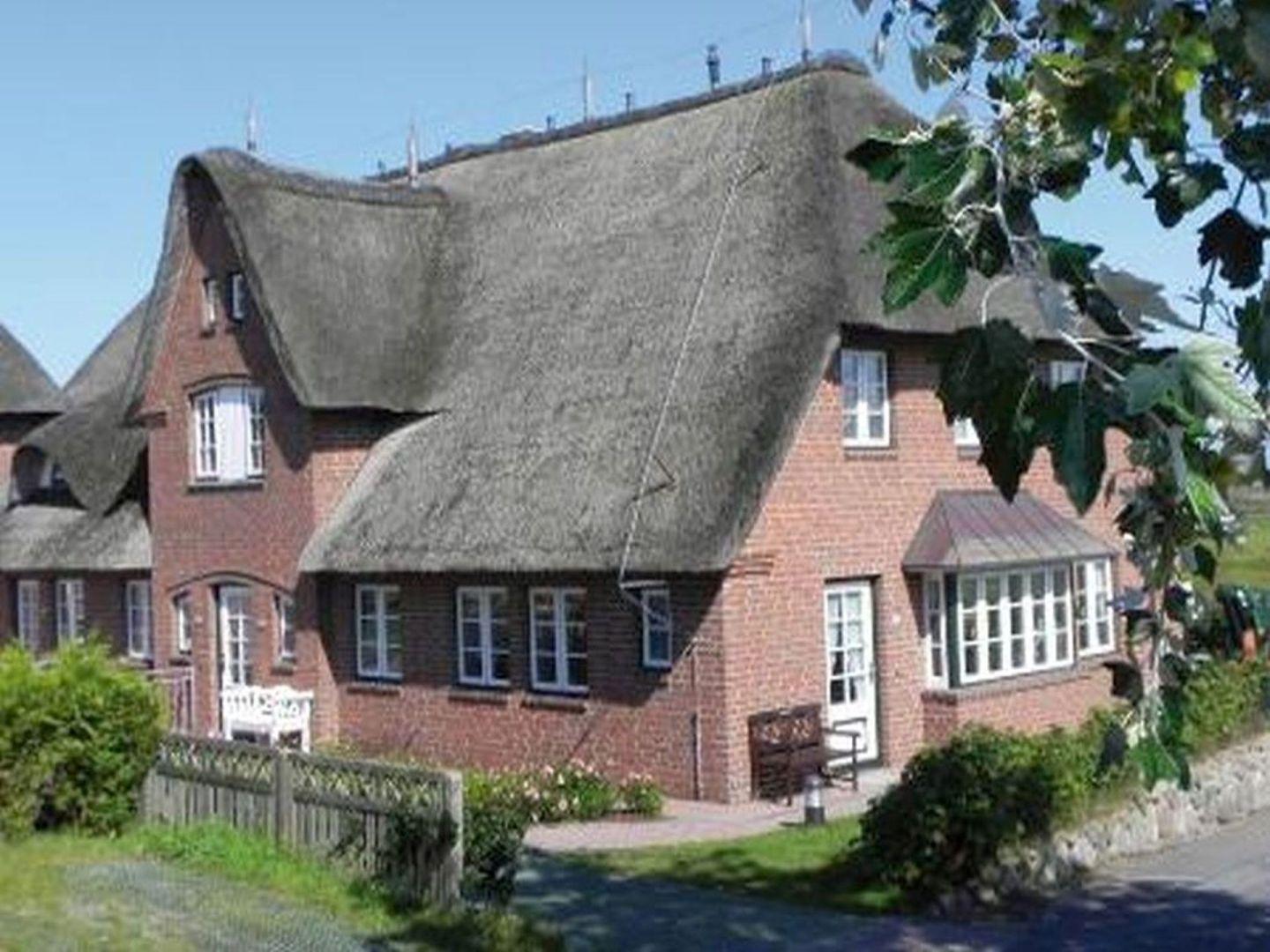 Rotes Backsteinhaus mit strohgedecktem Dach und weißen Fenstern.