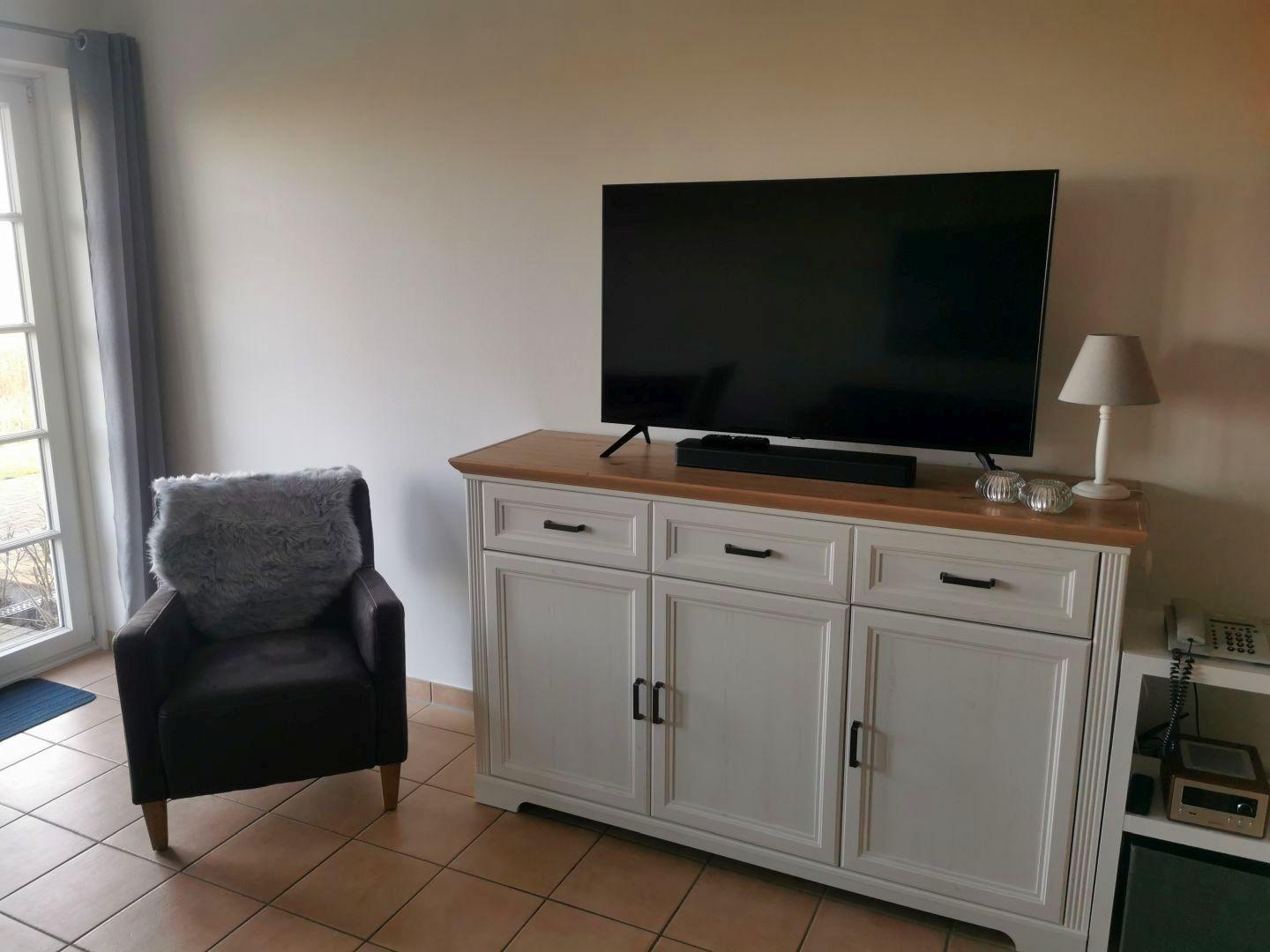 Ein Raum mit einem Fernseher auf einem weißen Schrank, einem schwarzen Sessel und einem Fenster.