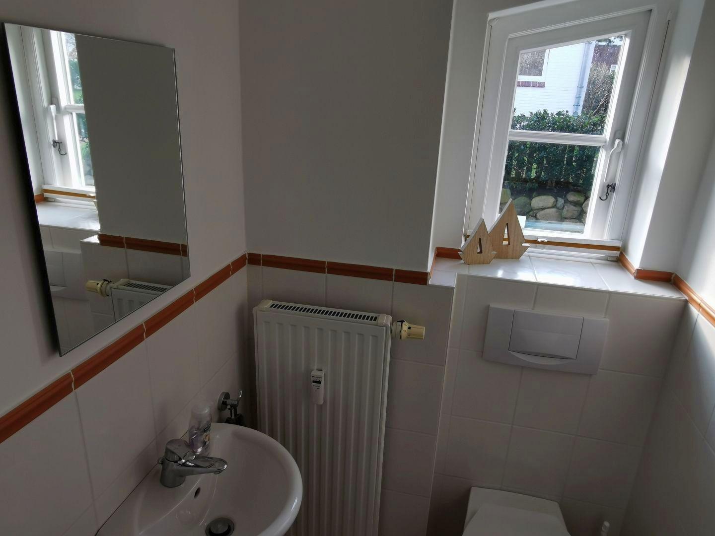 Badezimmer mit Waschbecken, Spiegel, Heizkörper und Fenster.