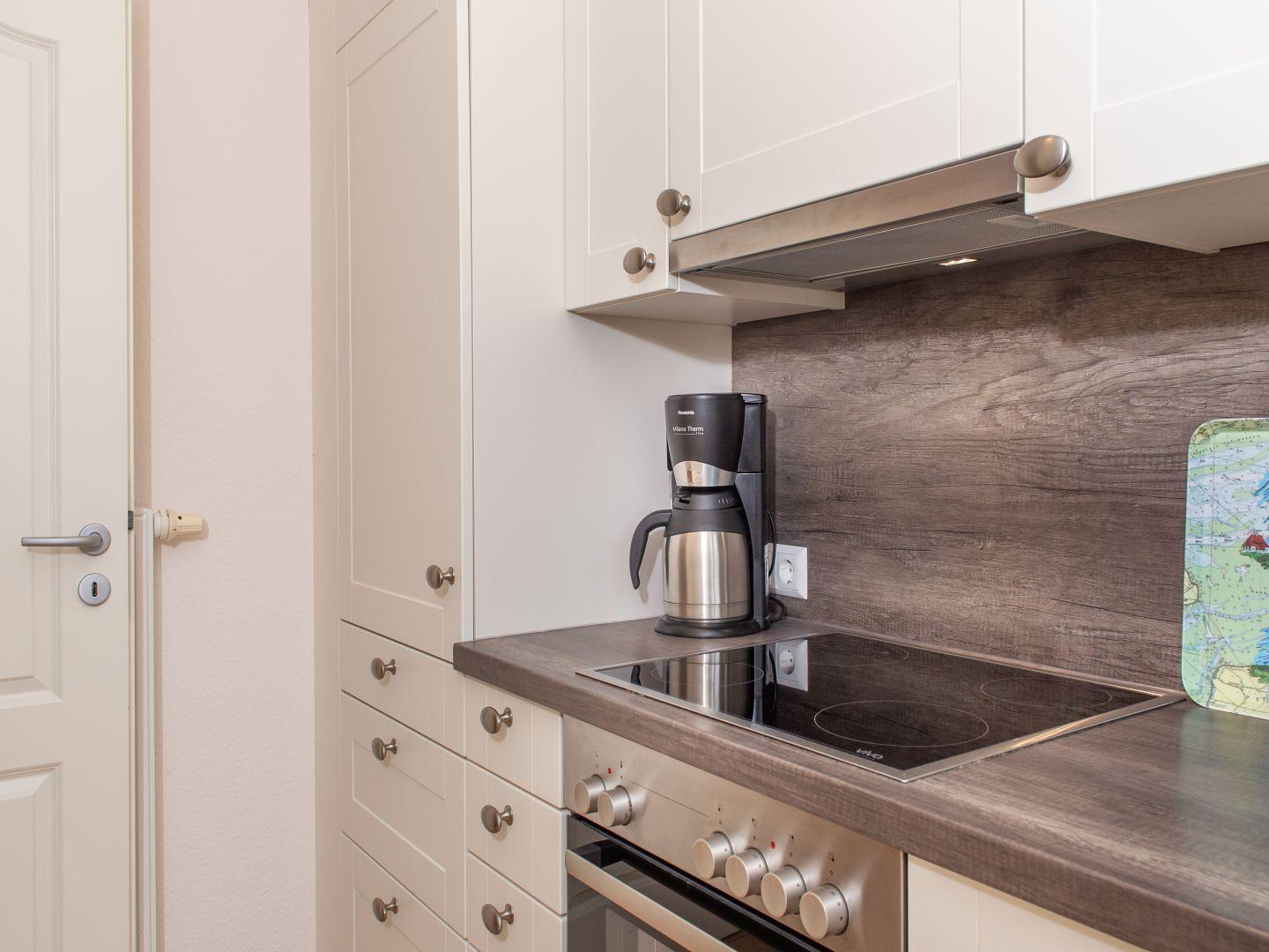 Küche mit Kochfeld, Kaffeemaschine und Holzrückwand.
