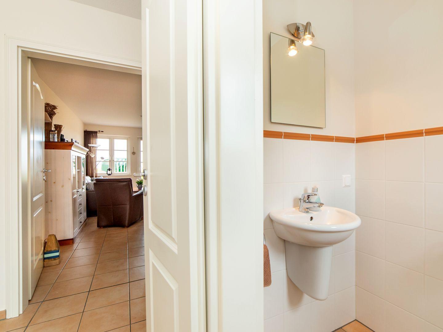 Badezimmer mit Waschbecken und Spiegel. Durchgang zum Wohnzimmer mit Sofa.