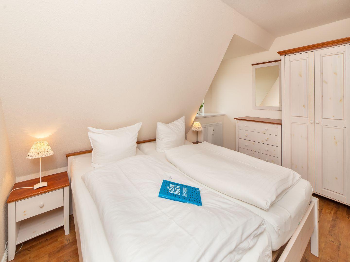 Schlafzimmer mit Doppelbett, Nachttisch, Kleiderschrank und Schreibtisch.