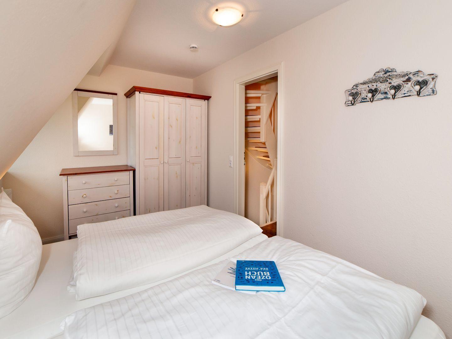 Schlafzimmer mit Doppelbett, Kleiderschrank und Bücherregal. Tür führt zur Treppe.