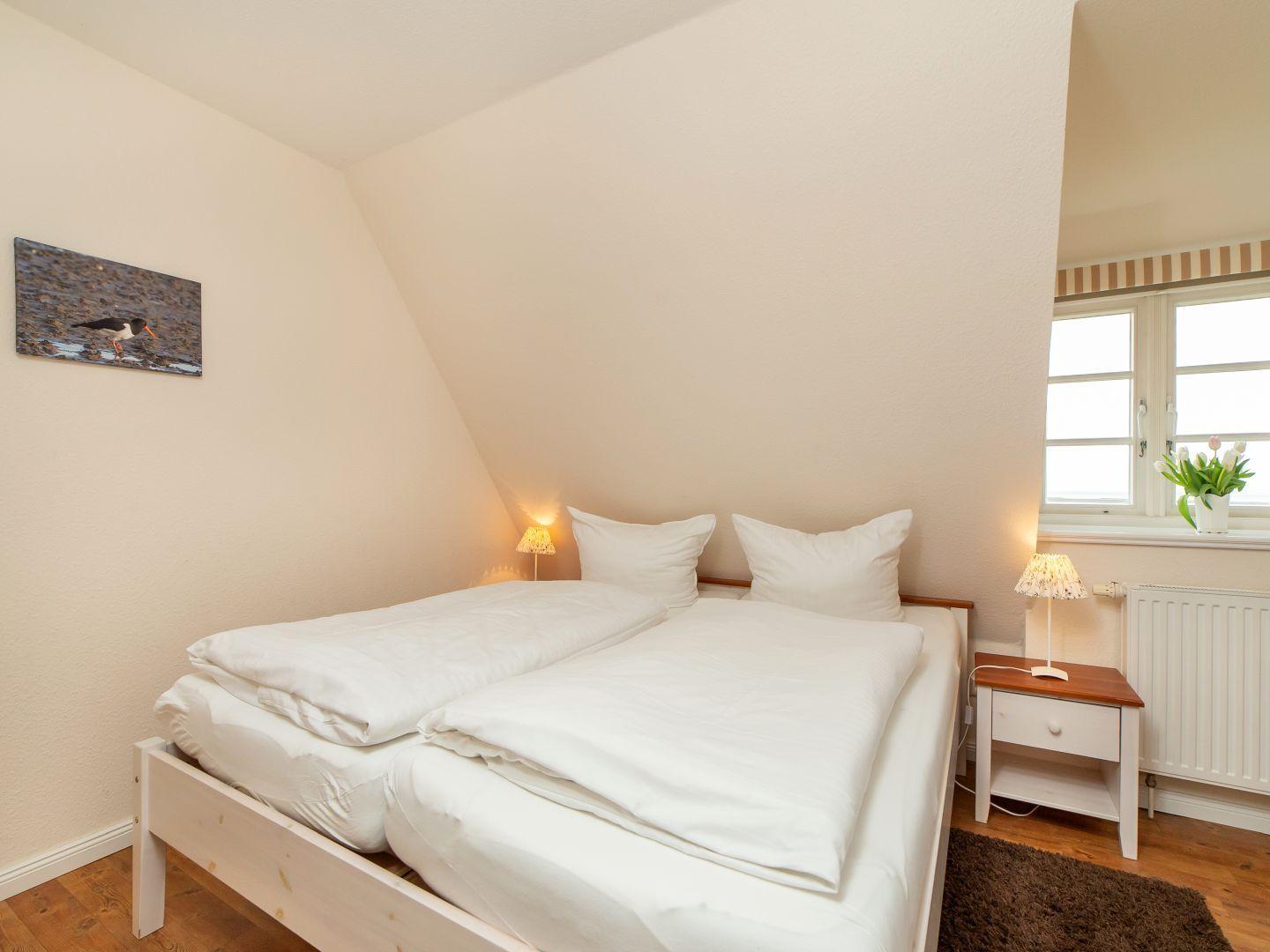Schlafzimmer mit Doppelbett, Nachttisch und Fenster.