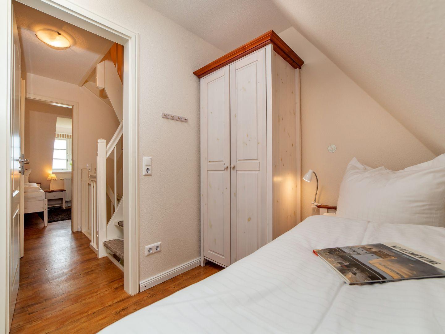 Schlafzimmer mit Dachschräge, weißem Schrank und Bett. Flur mit Treppe und weiterem Schlafzimmer.
