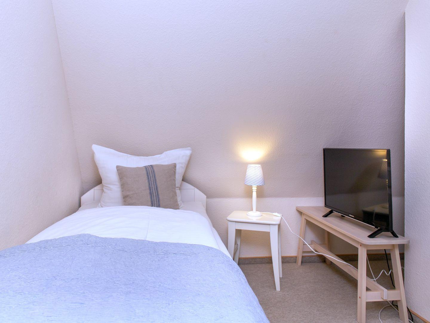 Ein Schlafzimmer mit Bett, Nachttisch, Lampe und Fernseher auf einem Tisch.