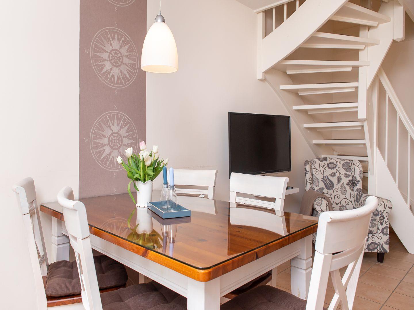Esszimmer mit Tisch, Stühlen, Fernseher und Treppe.