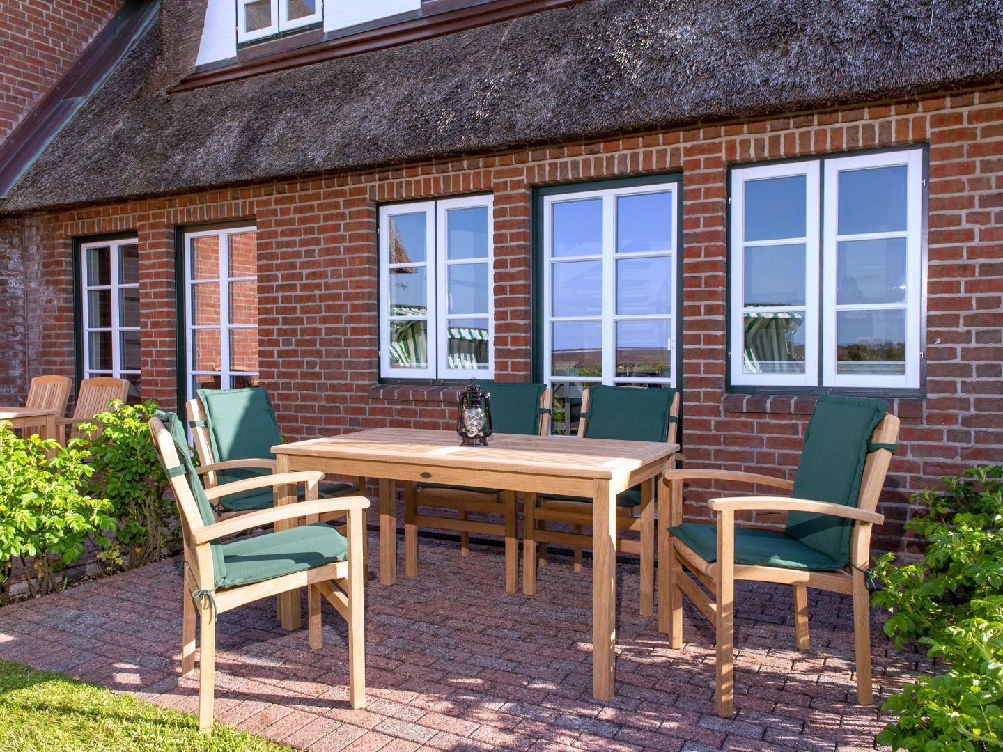 Terrasse mit Holztisch und Stühlen vor einem roten Backsteinhaus mit Strohdach.