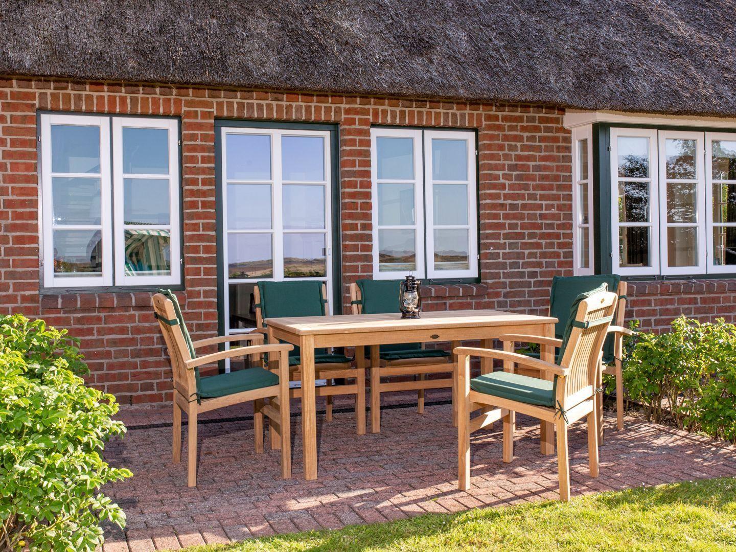 Terrasse mit Holztisch und Stühlen vor einem Backsteinhaus mit Strohdach.