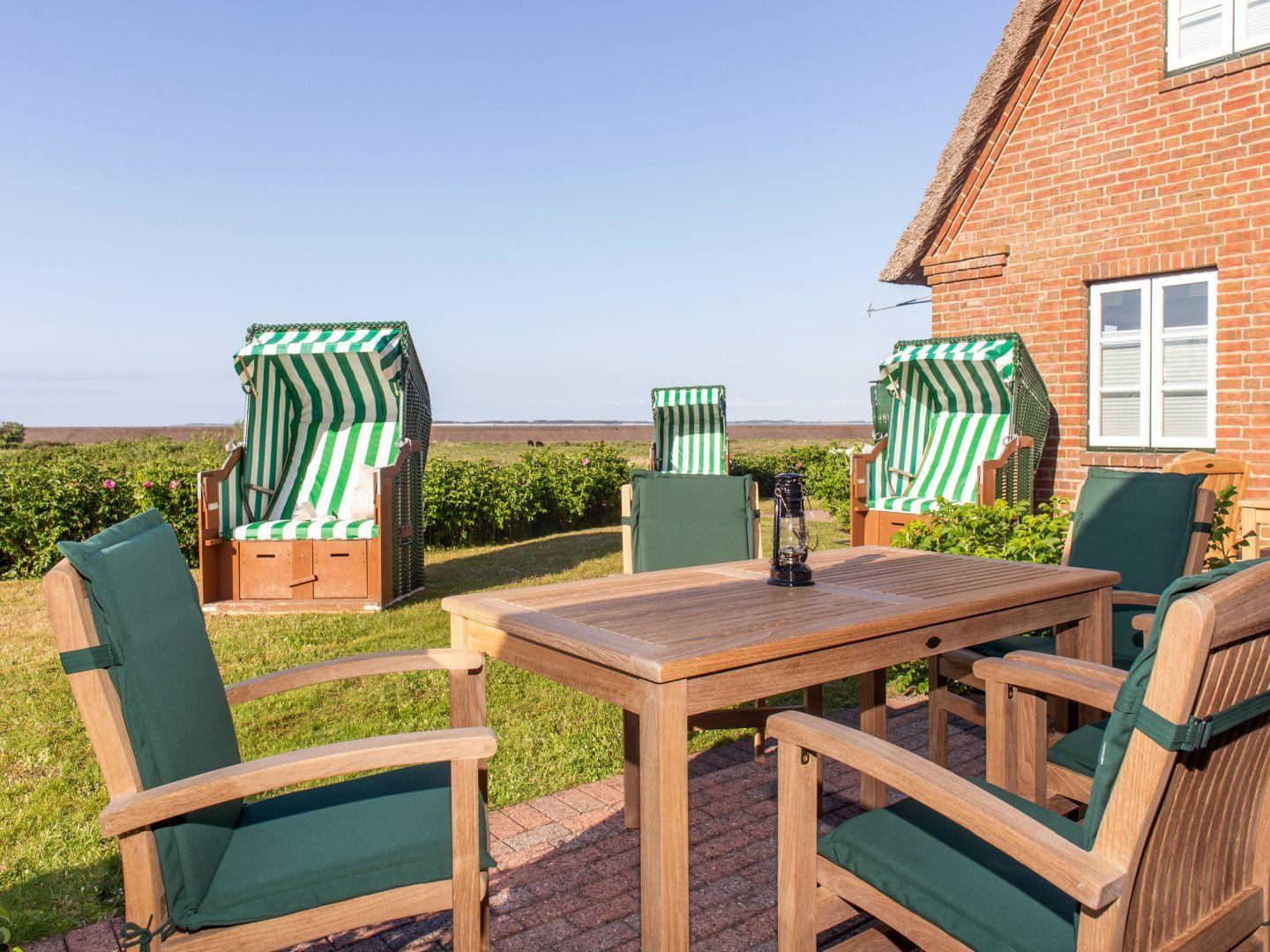 Terrasse mit Holztisch, Stühlen und Strandkörben. Blick auf Grünfläche und Haus.