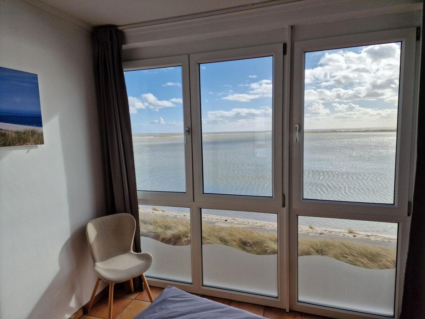 Zimmer mit Blick auf Strand und Meer durch große Fenster.