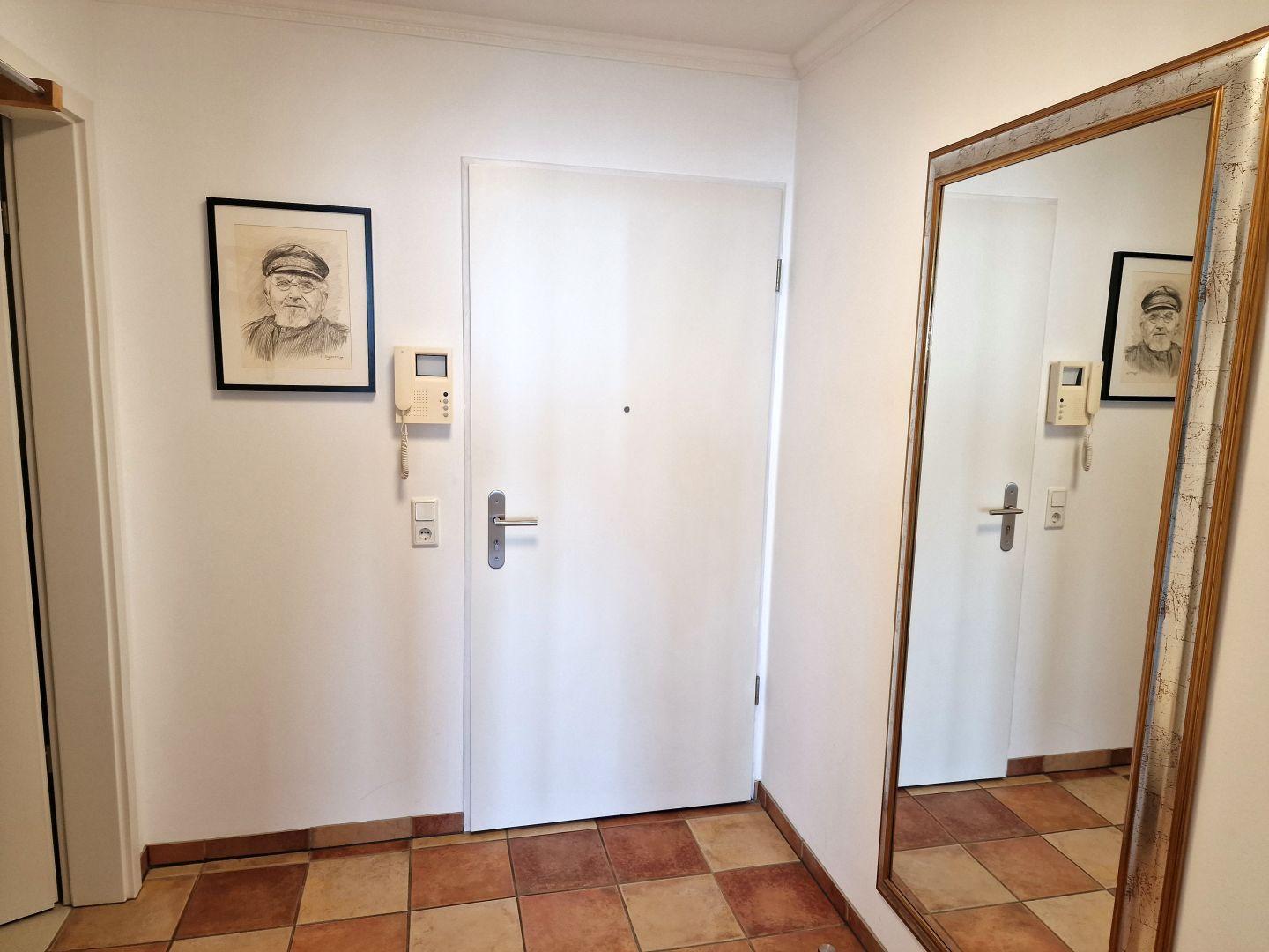 Eingangsbereich mit Tür, Spiegel und gerahmtem Bild an der Wand.