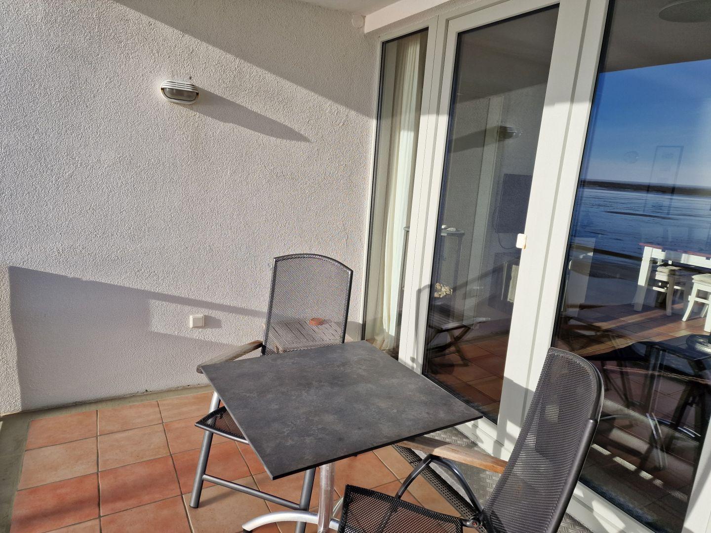 Terrasse mit Tisch und zwei Stühlen, Blick auf Wasser.