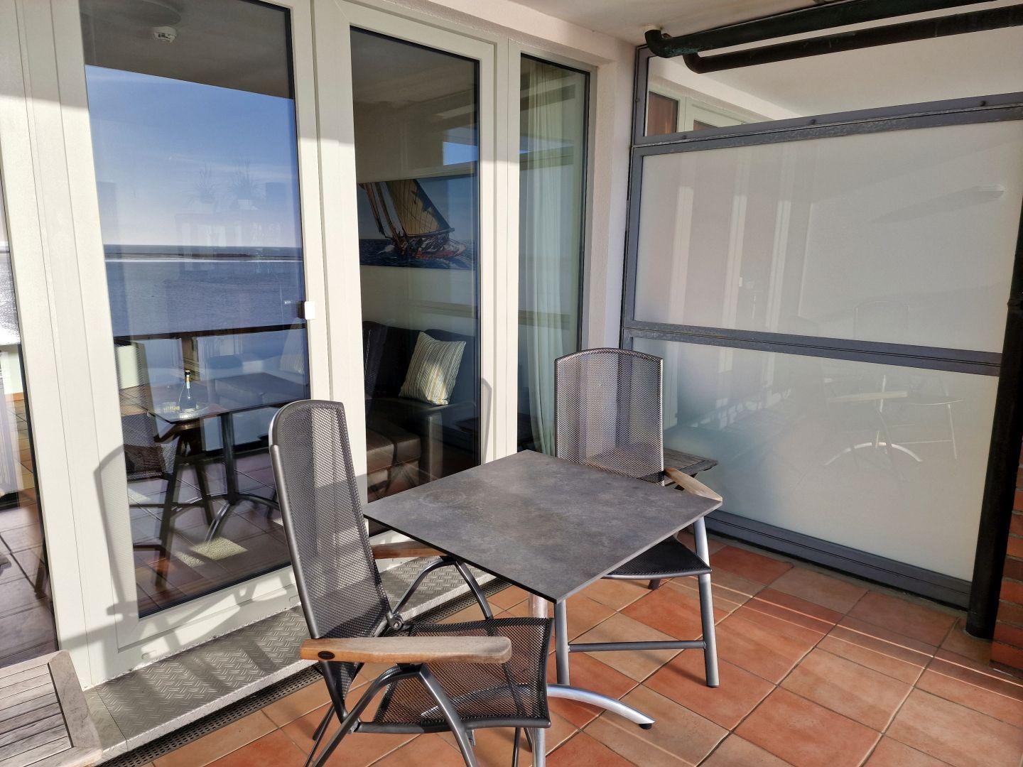 Terrasse mit Tisch und zwei Stühlen, Glaswand und Blick auf das Meer.