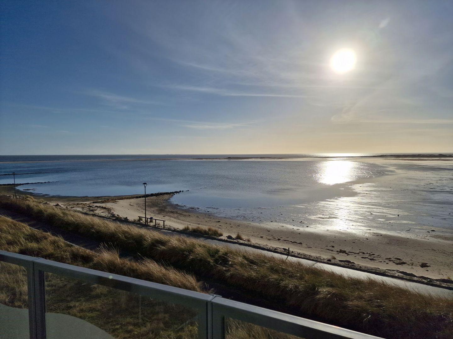 Blick auf Strand und Meer bei Sonnenaufgang mit Holzbank und Dünen.