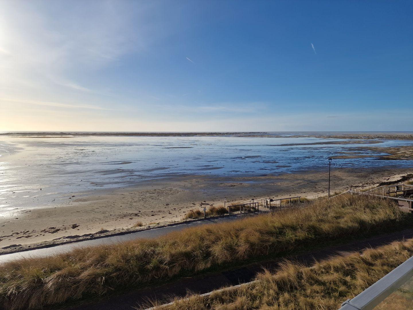 Weitläufiger Strand mit Wattgebieten und trockenem Uferbereich unter blauem Himmel.