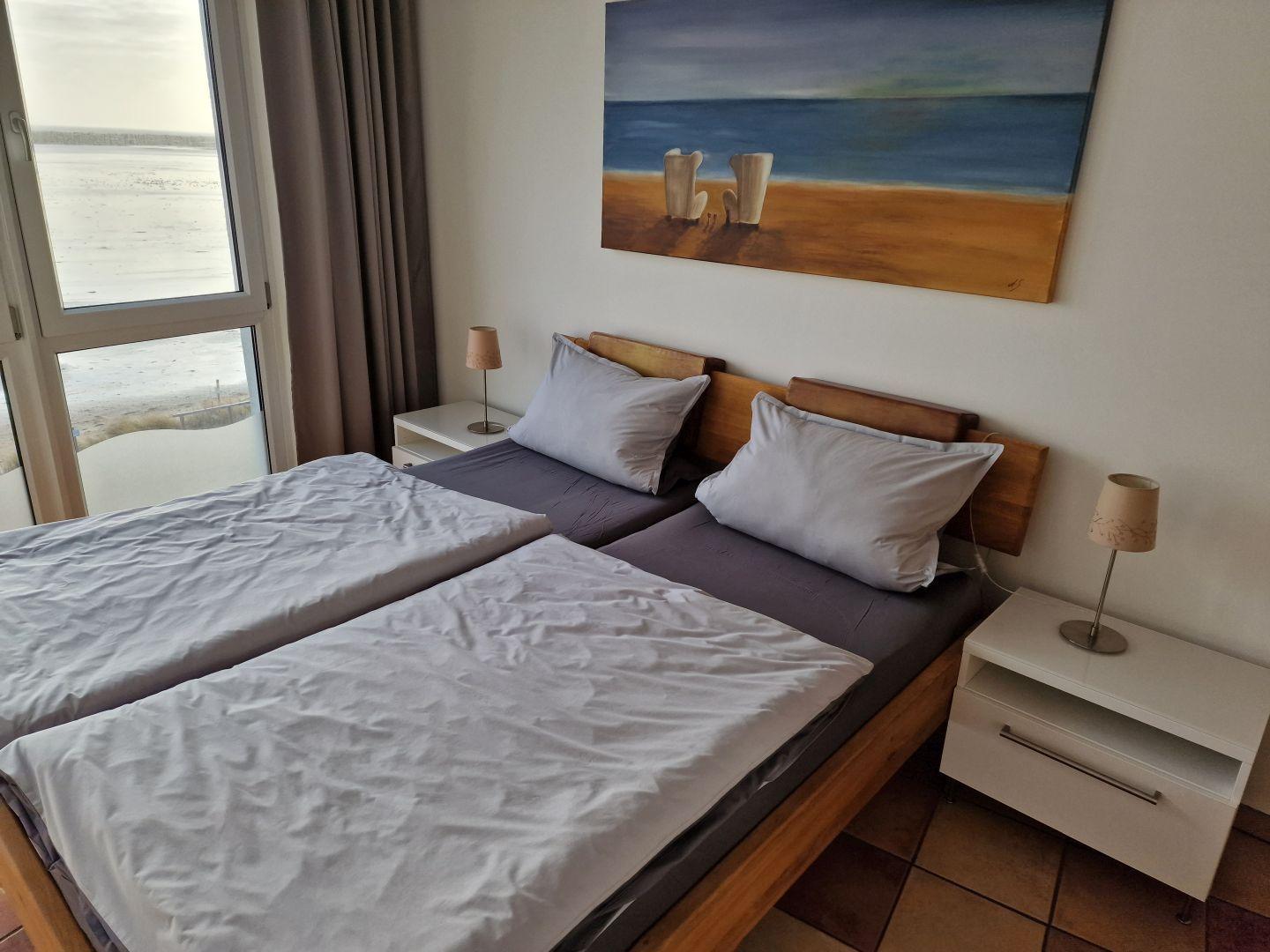 Schlafzimmer mit Doppelbett, zwei Nachttischen und Blick auf den Strand.