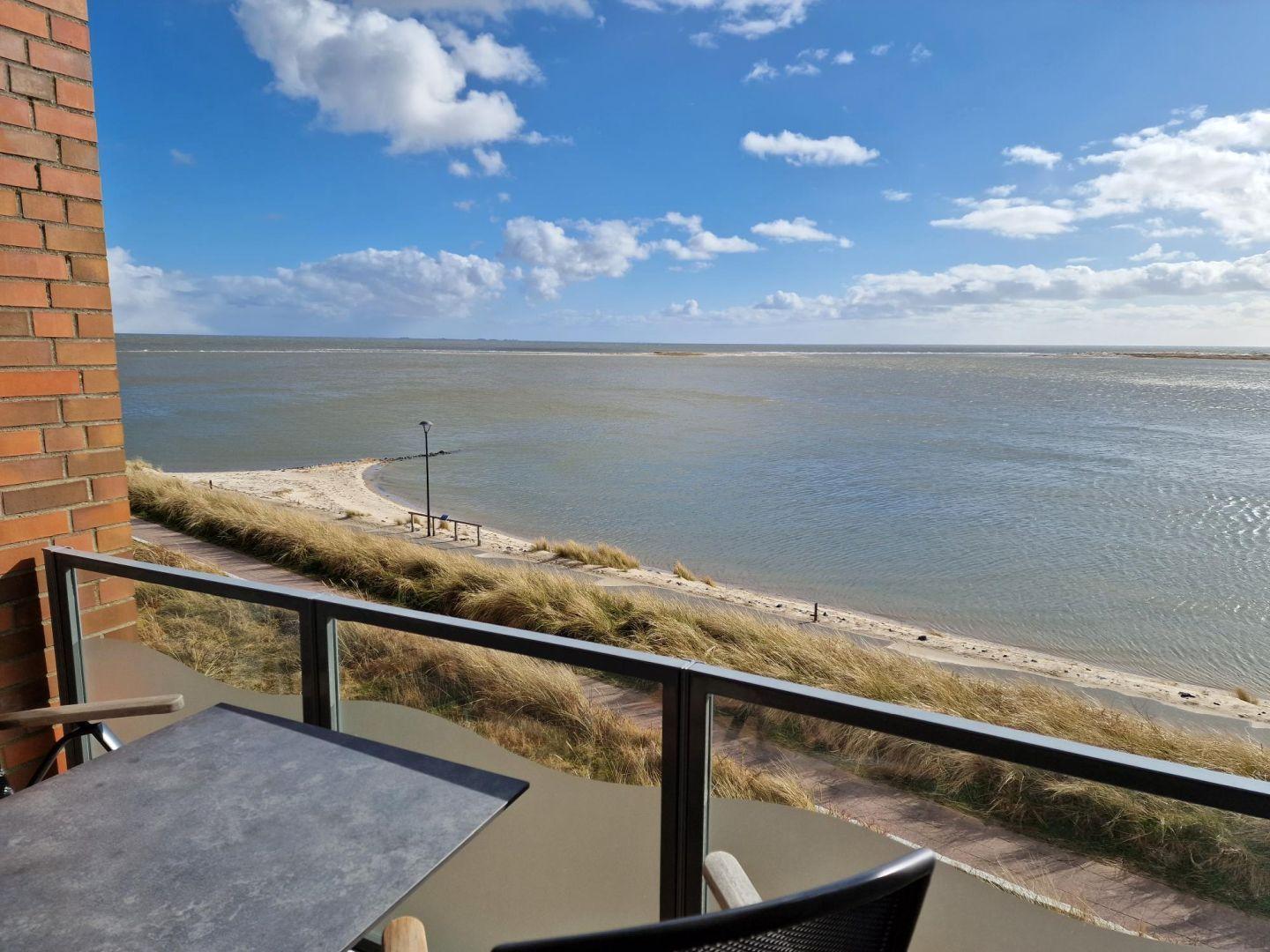Terrasse mit Tisch und Stühlen bietet Blick auf Strand und Meer.