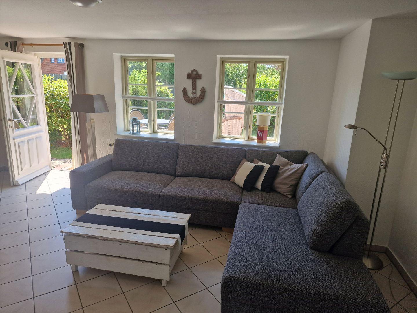 Wohnzimmer mit grauem Sofa, weißen Fenstern und Terrassentür.
