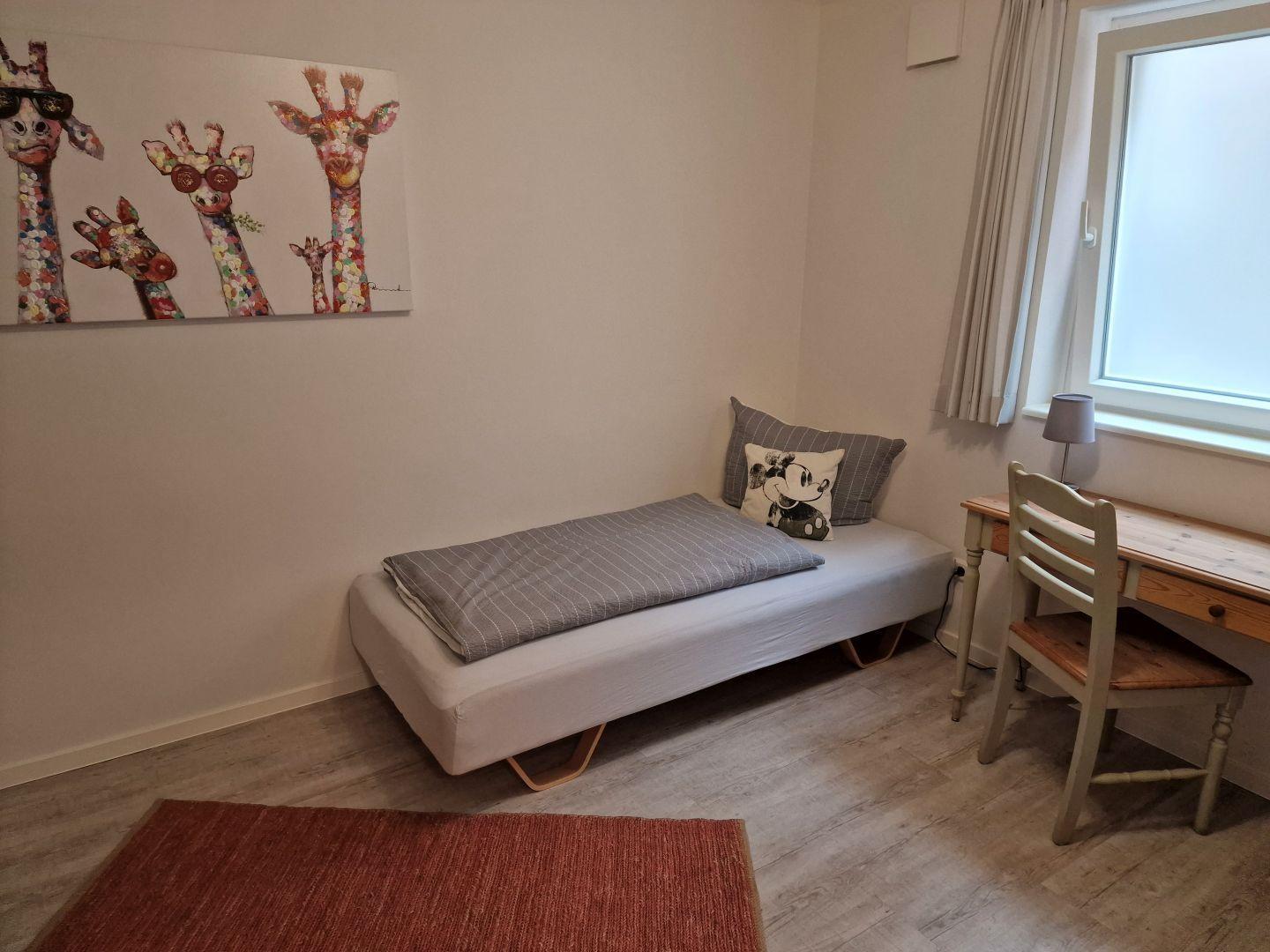 Schlafzimmer mit Bett, Schreibtisch und Wandbild mit Giraffen.