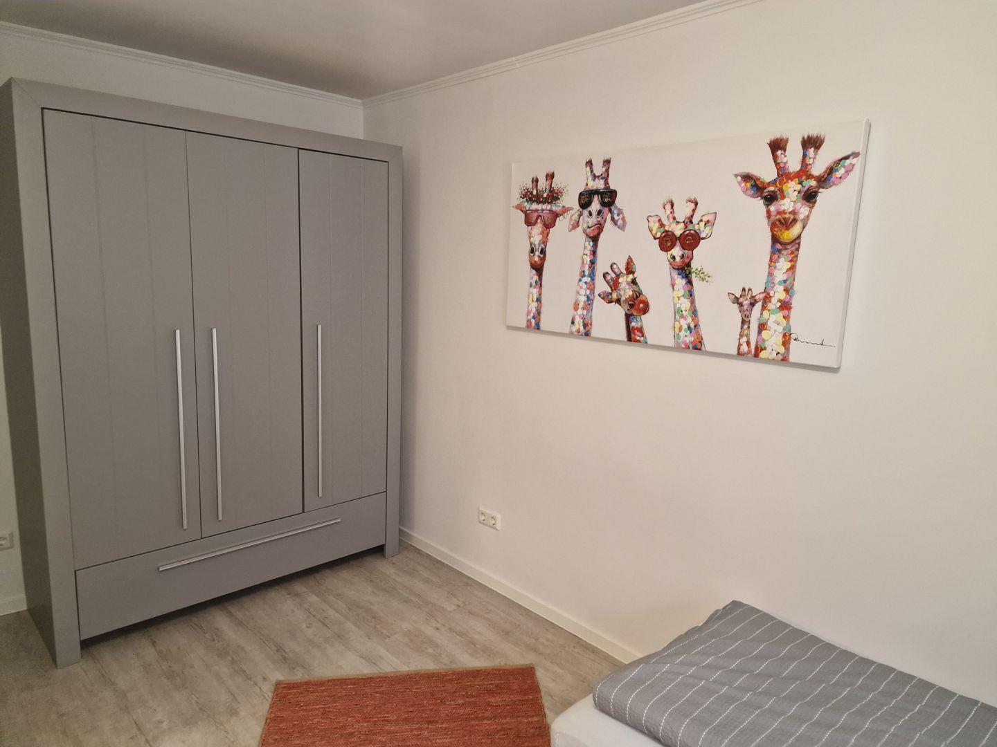 Schlafzimmer mit Kleiderschrank und Giraffenbild an der Wand.