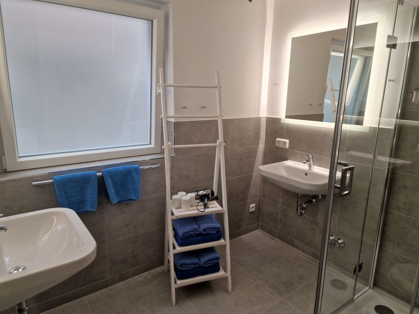 Badezimmer mit Dusche, Waschbecken und blauen Handtüchern.