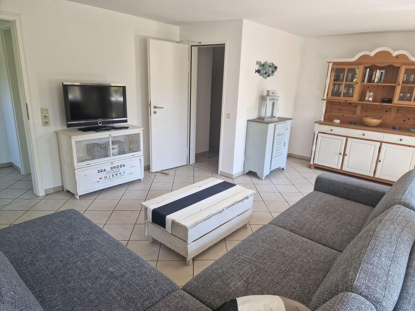 Wohnzimmer mit Sofa, Couchtisch, Fernseher und Schränken.