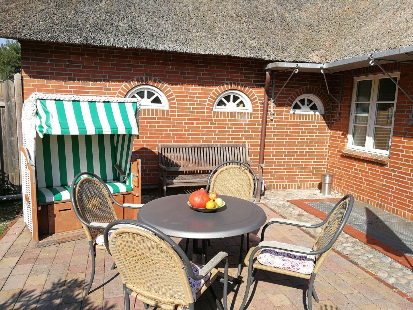 Terrasse mit Tisch, Stühlen und Strandkorb vor Backsteinhaus mit Dach