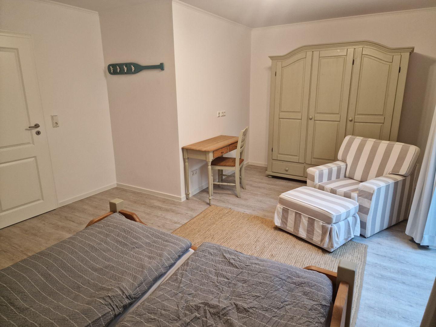 Zimmer mit Doppelbett, Schreibtisch, Sessel und Kleiderschrank.
