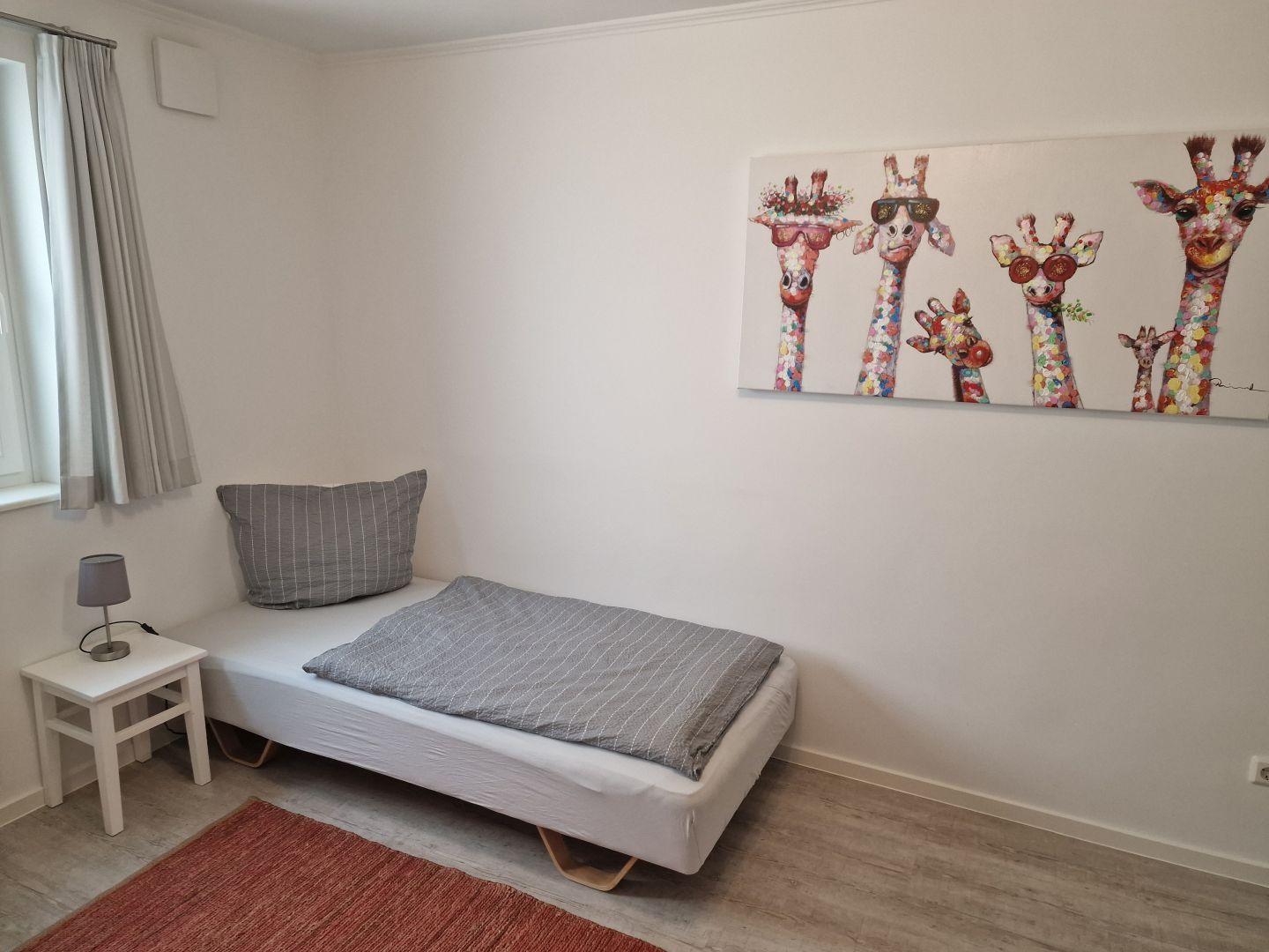Ein Schlafzimmer mit Bett, Nachttisch und Wandbild mit Giraffen.