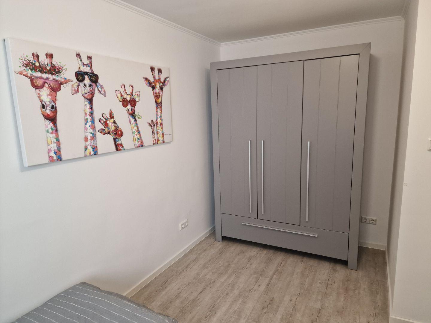 Schlafzimmer mit Kleiderschrank und Giraffenbild an der Wand.