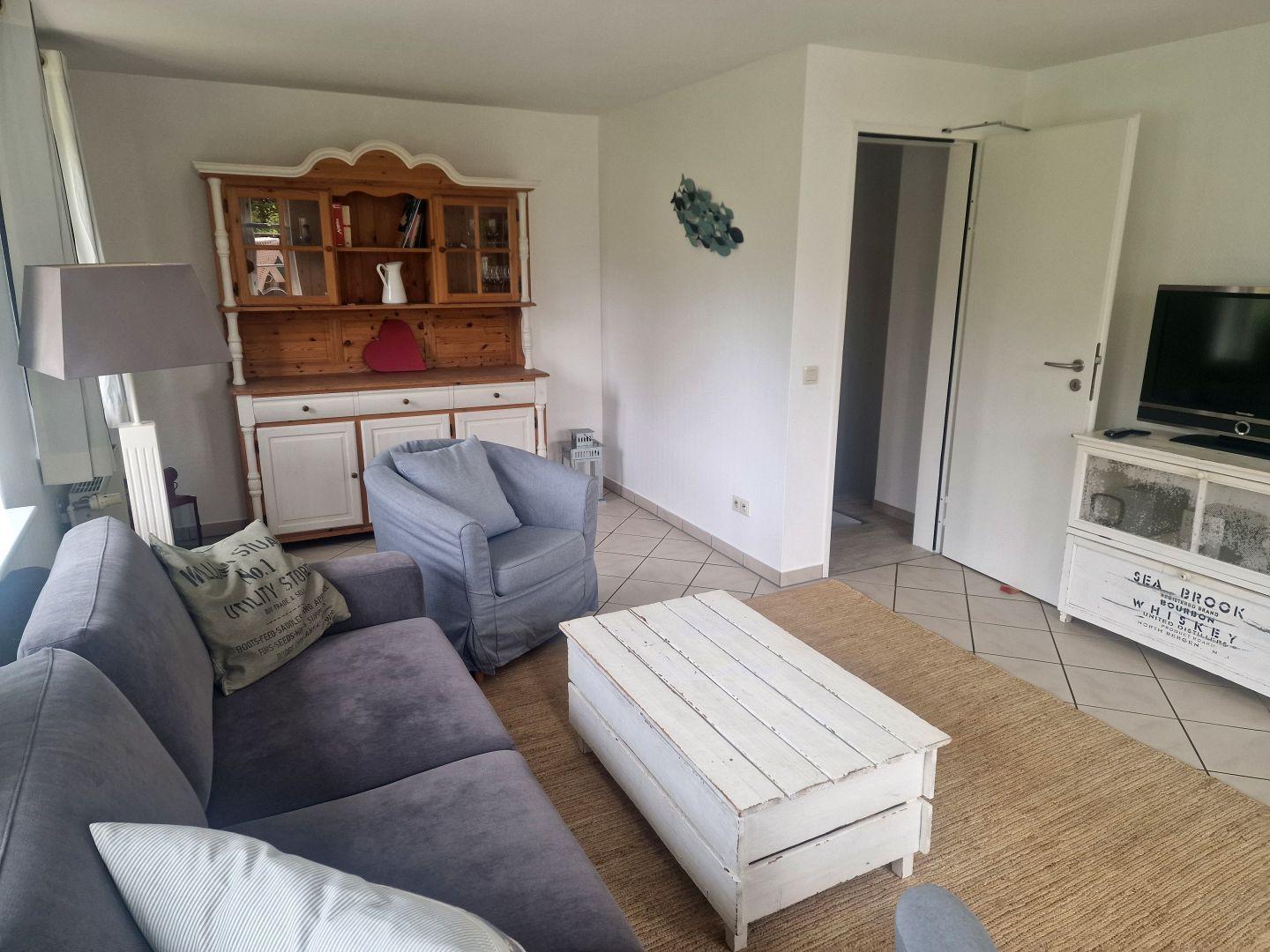 Wohnzimmer mit Sofa, Sessel, Couchtisch und TV.